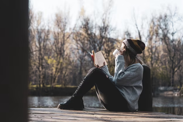 Young woman sitting on a pier above a lake and reading a book